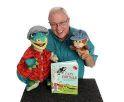 image features the performer, Mark Daniels (an older gentleman) holding two of his puppets that look like dinosaurs. There is a book set up on a table in front of them.